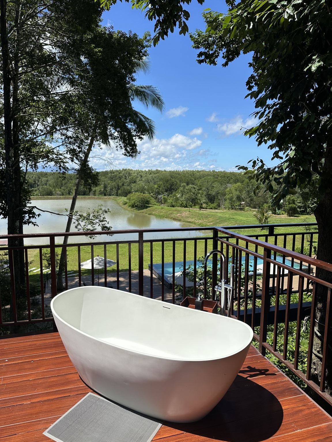 Outdoor bathtub on a wooden deck surrounded by tropical greenery